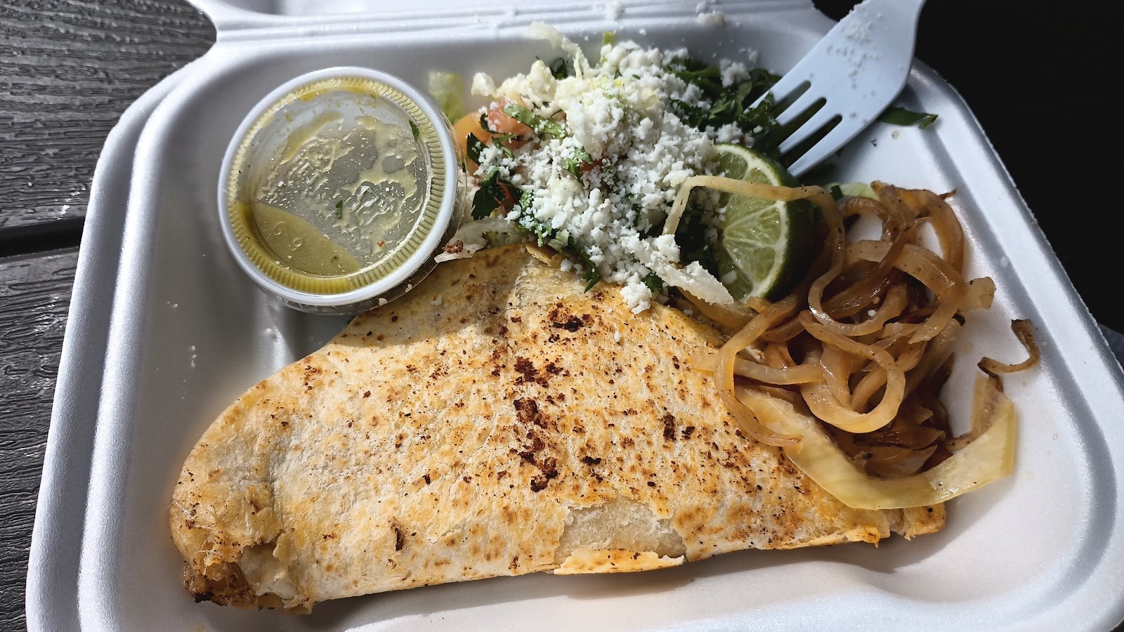 A grilled fish quesadilla with sautéed onions, fresh salad, queso fresco and salsa verde