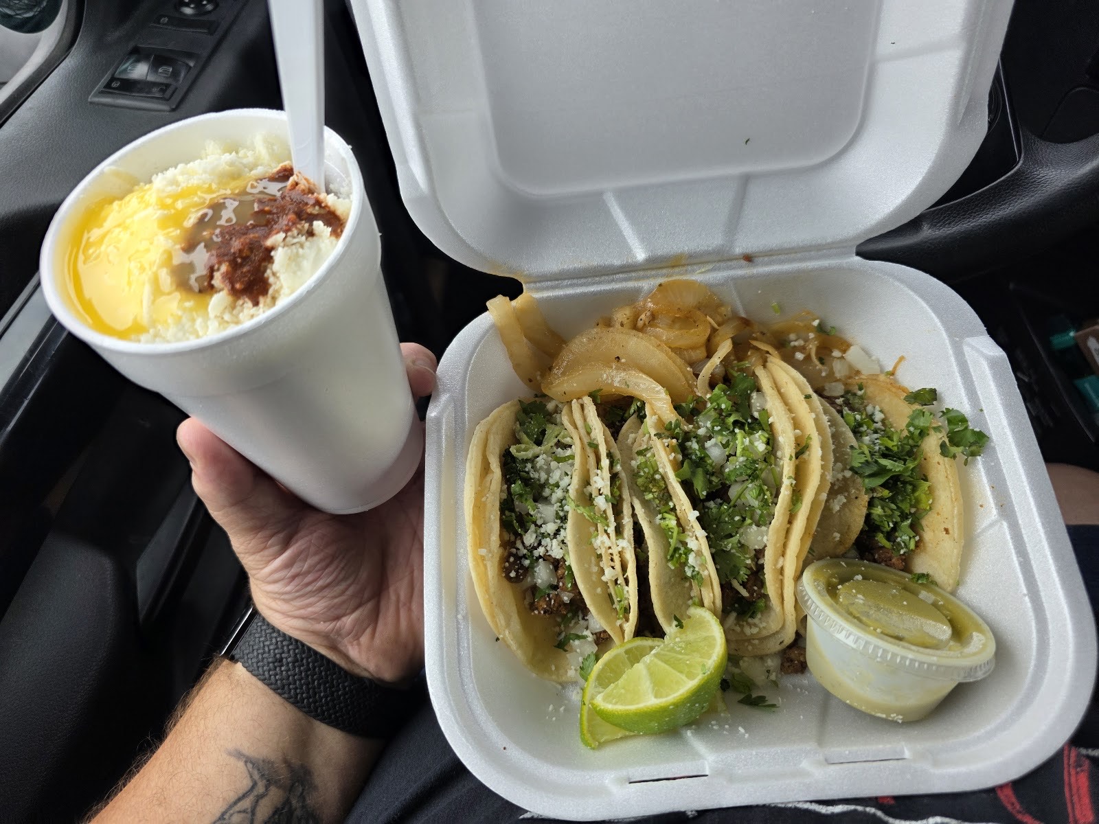 A tray of Gueros Tacos street tacos with cilantro, onion and lime beside a cup of creamy elote, held fresh from the truck window in Bradenton, Florida
